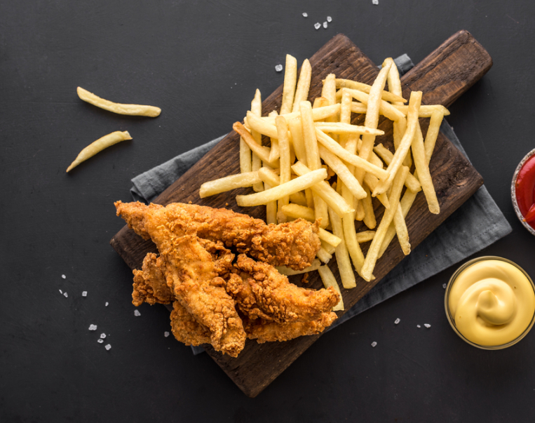 Fish and chips. Deep fried fish filet and with french fries served on black table with sauces. Traditional british street food, top view, copy space.